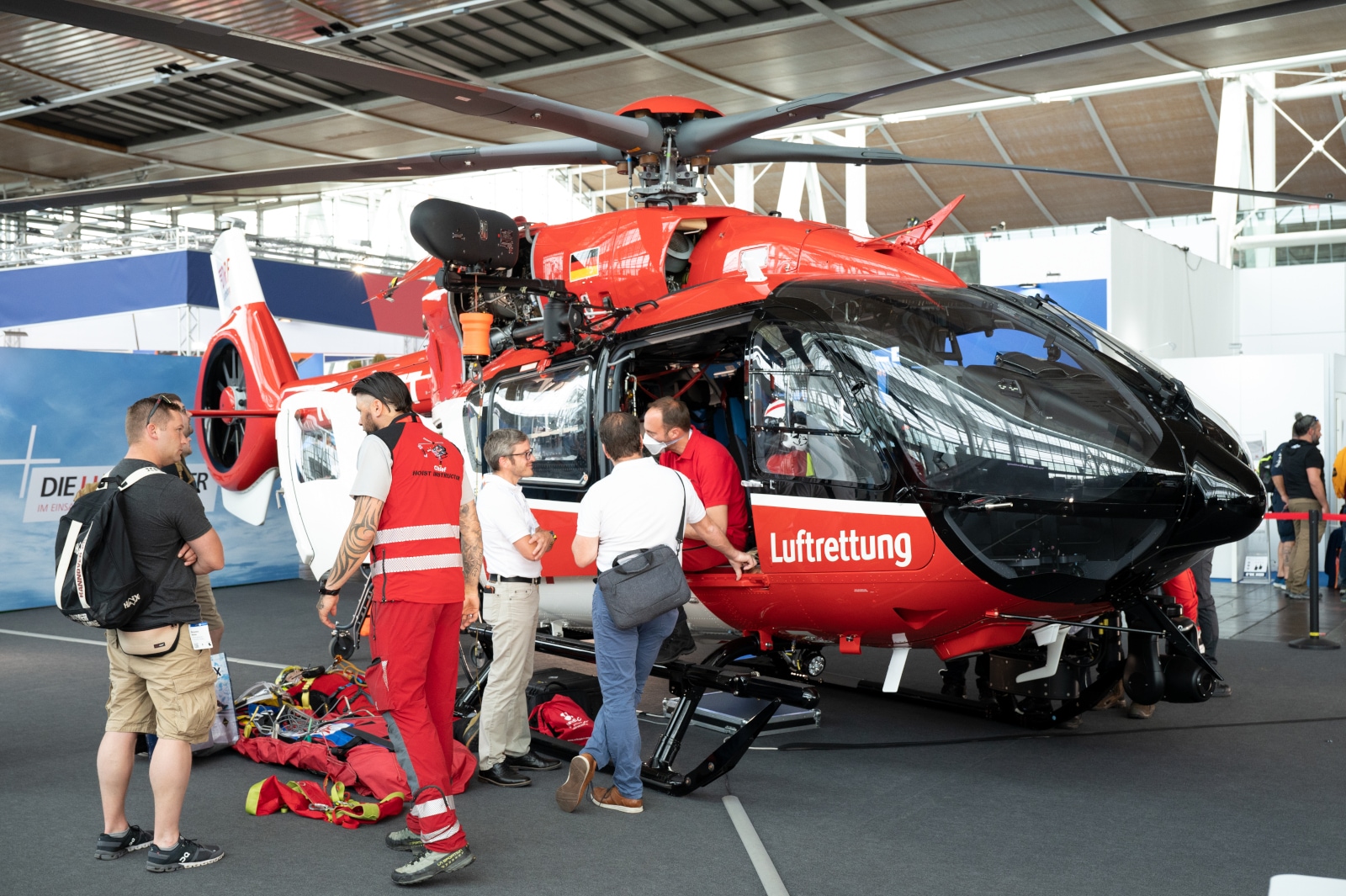 Ein orangefarbener Helikopter der Flugrettung steht auf einem INTERSCHUTZ Stand. Davor stehen Mitarbeiter, die sich mit Besuchern unterhalten