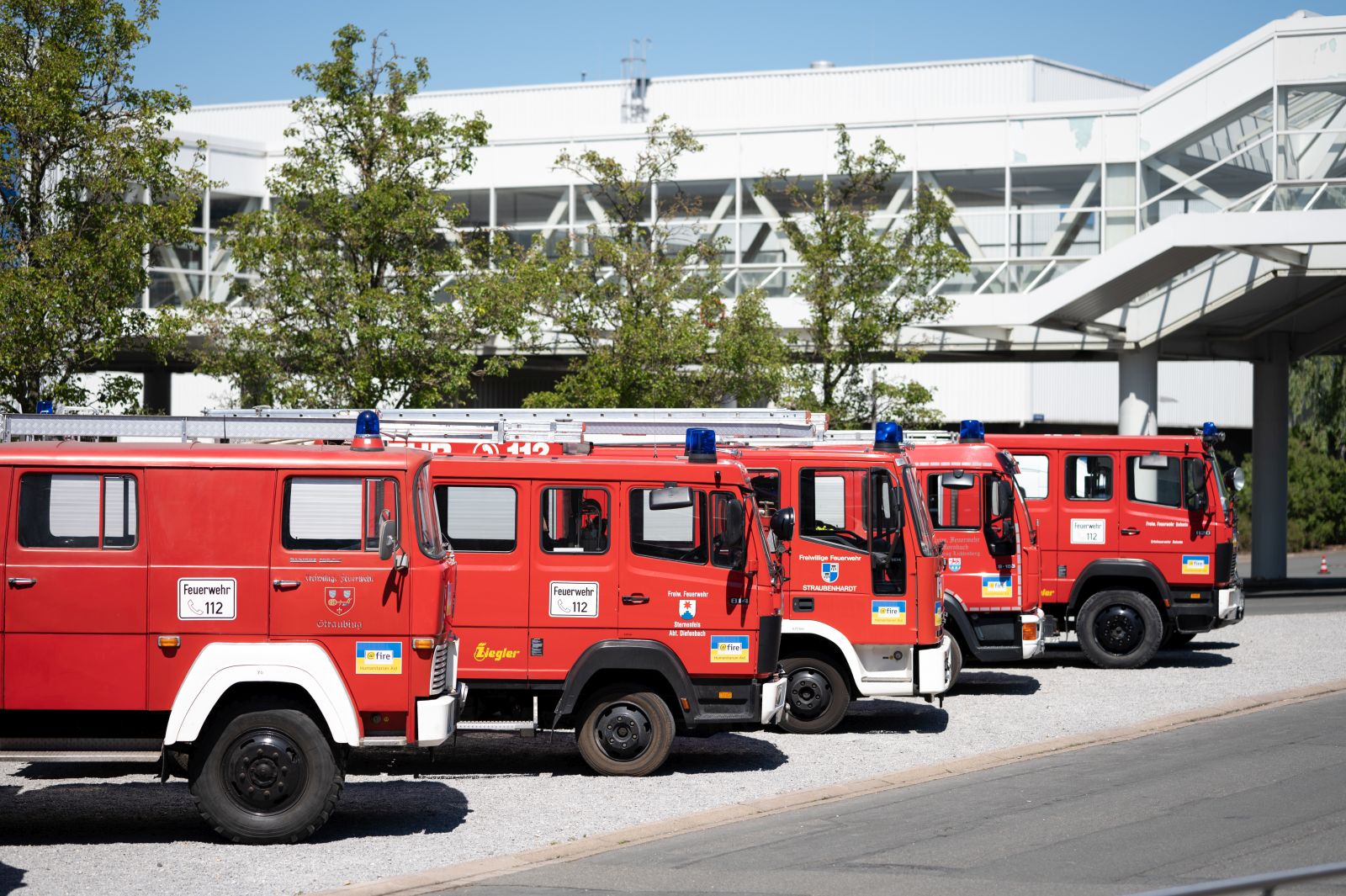 Five red fire trucks are displayed in a row on the outdoor grounds.